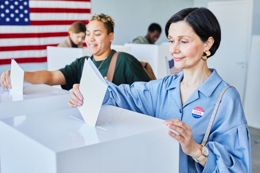 Portrait of smiling American woman voting and putting ballot in bin on election day